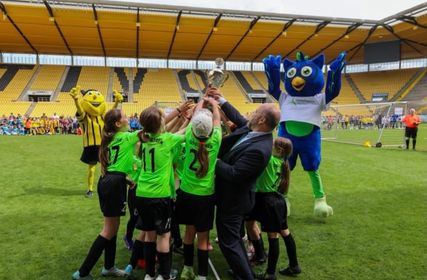 Auf dem heiligen Rasen des Aachener Tivoli kürte Oberbürgermeister Michael Ziemons die Mädchen der GGS Roetgen zu den Siegern der Grundschulemeisterscahft im Fußball. Alemannia-Maskottchen »Al-Aix« jubelt mit. Für das Maskottchen (r.) der Städteregion Aachen wird noch ein Name gesucht.