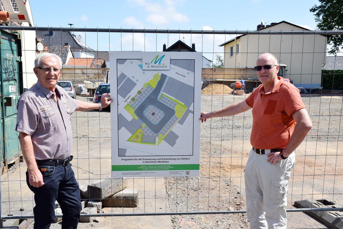 Ortsvorsteher Rolf Jaeck (l.) und Christof Marx, Diplom-Ingenieur für Landschaftspflege der Stadt Mechernich, zeigen den Plan zur Neugestaltung des Arenbergplatzes, der am Bauzaun vor Ort für alle einsehbar ist. Foto: Kirsten Röder/pp/Agentur ProfiPress