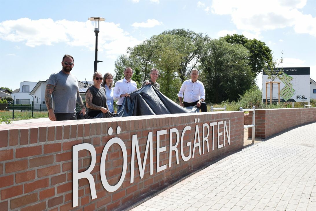 Enthüllten den Römergärten-Schriftzug am Quartiersplatz im Neubaugebiet »Römergärten« (v.r.): Bürgermeister Ulf Hürtgen, Stadtplaner Christoph M. Hartmann, Prokurist Jan Radermacher und Rebecca Hirschmann von der Firma »F&amp;S concept« sowie Christina und Andreas Knappe von der Firma »Knappe + Team - Im Prin(t)zip Druck!«.