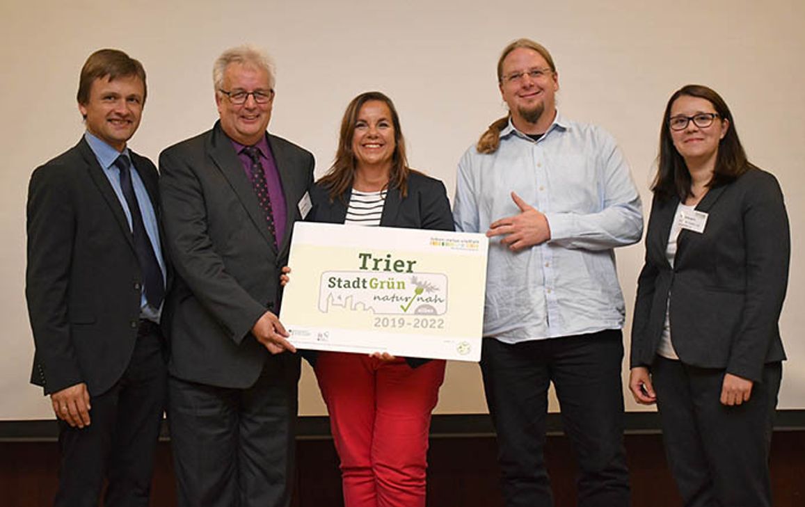 Robert Spreter, Geschäftsführer "Kommunen für biologische Vielfalt" (l.), und Deliana Bungard (Deutscher Städte- und Gemeindebund, r.) überreichen das Label "Stadtgrün naturnah" in Silber an Baudezernent Andreas Ludwig, Christine-Petra Schacht (Leiterin Stadtgrün Trier) und Christian Thesen (Mitarbeiter Stadtgrün Trier). Foto: Sascha Engst