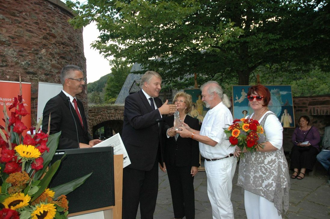 Landrat Wolfgang Spelthahn (2.v.l.) überreicht Herb Schiffer die gläserne Löwen-Skulptur, Uwe Zimmermann (l., Sparkasse Düren) hält den symbolischen Scheck über 5000 Euro bereit. Zu den ersten Gratulanten zählten die Kultur-Politikerin Käthe Rolfink und Schiffers Ehefrau Anne (r.).
