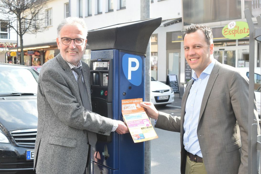 Bürgermeister Dr. Uwe Friedl und Sacha Reichelt, Fachbereichsleiter Recht und Ordnung, haben am Parkautomaten in der Wilhelmstraße einen  Aufkleber mit allen nützlichen Infos zum Handyparken angebracht. An den weiteren 84 Automaten wird ebenfalls ein solcher Hinweis angebracht.Foto: Anja Breuer