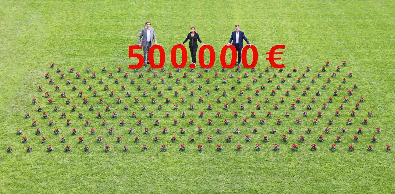 Stellvertretend für jeden Empfängerverein steht eine rotblühende Pflanze auf dem Rasen. Herzlich gratulieren Norbert Laufs, Vorstandsvorsitzender der Sparkasse Aachen, Susanne Schwier vom Vorstand der Jugend- und Kulturstiftung und Dr. Christian Burmester, Vorstandsvorsitzender der Kulturstiftung (v. l. n. r.)