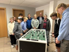 Jugendliche beim Tischkicker spielen sowie Initiatorin Olga Veresokin, Ortsbürgermeister Manuel Weber, Beigeordneter Bernhard Werle und OIE Vorstand Thomas Johann