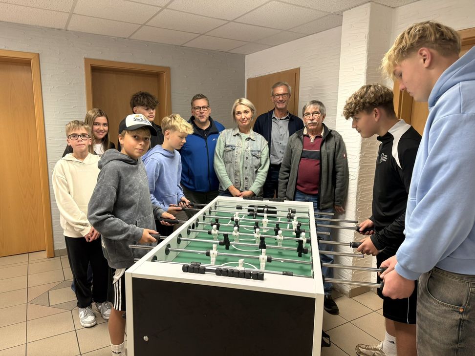 Jugendliche beim Tischkicker spielen sowie Initiatorin Olga Veresokin, Ortsbürgermeister Manuel Weber, Beigeordneter Bernhard Werle und OIE Vorstand Thomas Johann