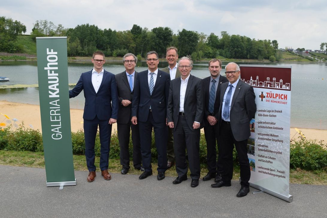 Bei einer Pressekonferenz, zu der Bürgermeister Ulf Hürtgen (3.v.r.) geladen hatte, stellten  Klaus Hellmich, Geschäftsführer Digital und Logistik der Galeria Kaufhof GmbH, und sein Team das Bauvorhaben vor.  Foto: Breuer, Animation: Fiege/AJS