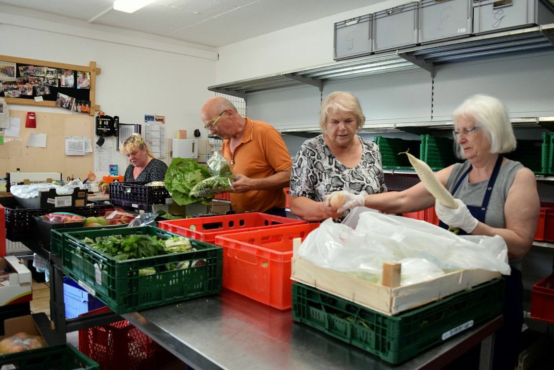 Sabine Henze gibt nur von hinter der eigens aufgestellten Plexiglas-Scheibe die Ware aus. Mechernichs Tafel-Chef Wolfgang Weilerswist freut sich über den guten Start nach der Corona-Zwangspause. Foto: Kirsten Röder/pp/Agentur