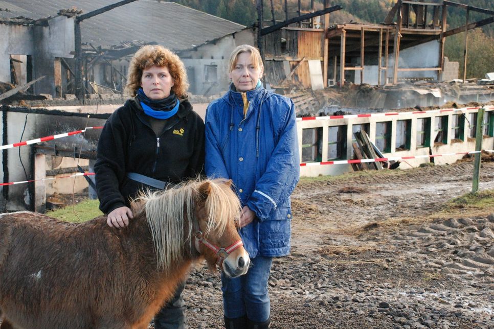 Pächterin Monika Ley (l.) und Julietta Kahlbetzer vor der abgebrannten Ruine des Reiterhofes. Wie lang es dauern wird, bis der Gelände wieder nutzbar ist, weiß zur Zeit noch niemand. Foto: Nolden