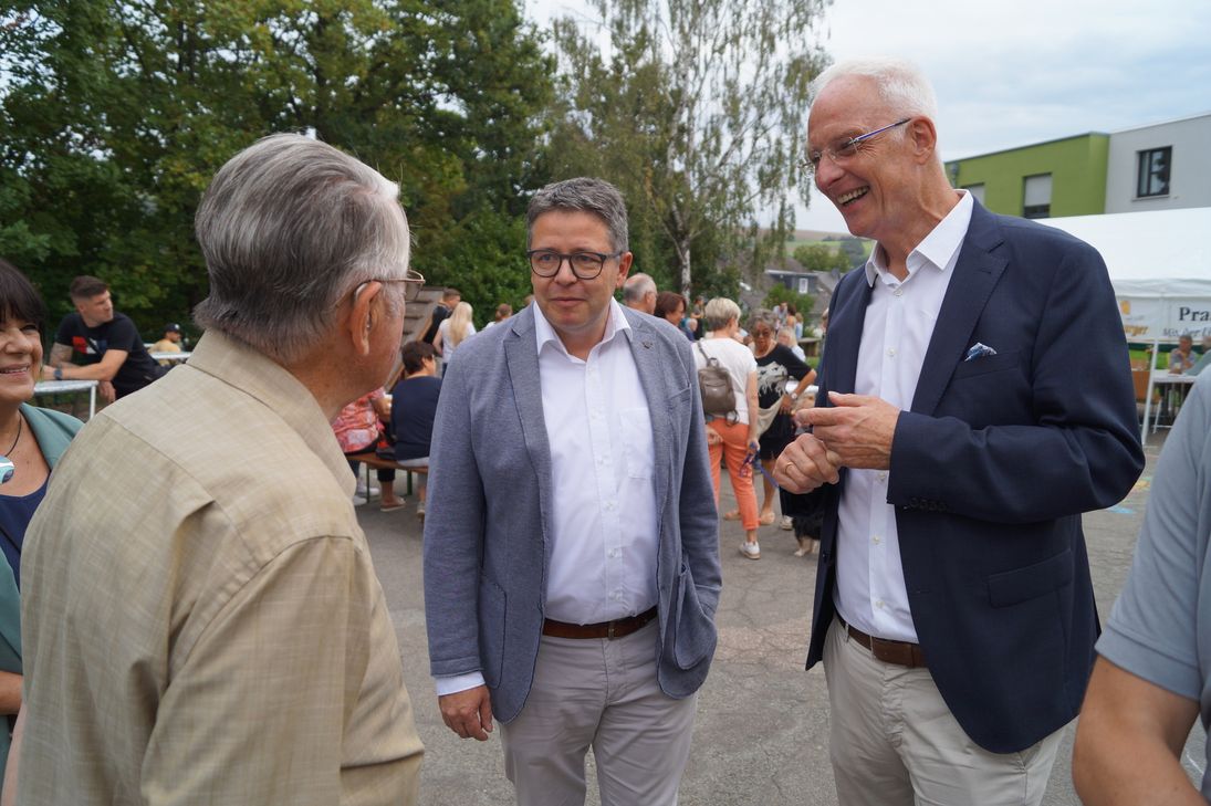 "Marco van Elkan, Referatsleiter im rheinland-pfälzischen Innenministerium (links) und Triers Oberbürgermeister Wolfram Leibe (rechts) im Gespräch mit Besuchern des Stadtdorffestes in Kernscheid."