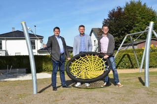 Bennet Gielen (Beigeordneter der Gemeinde Simmerath), Ortsvorsteher Marc Topp und Marcel Wüller (Tiefbauamt) präsentieren den neuen Spielplatz in Rollesbroich. Die Nestschaukel ist eines der neuen Spielgeräte direkt neben dem im Bau befindlichen Feuerwehrhaus. Foto: T. Förster