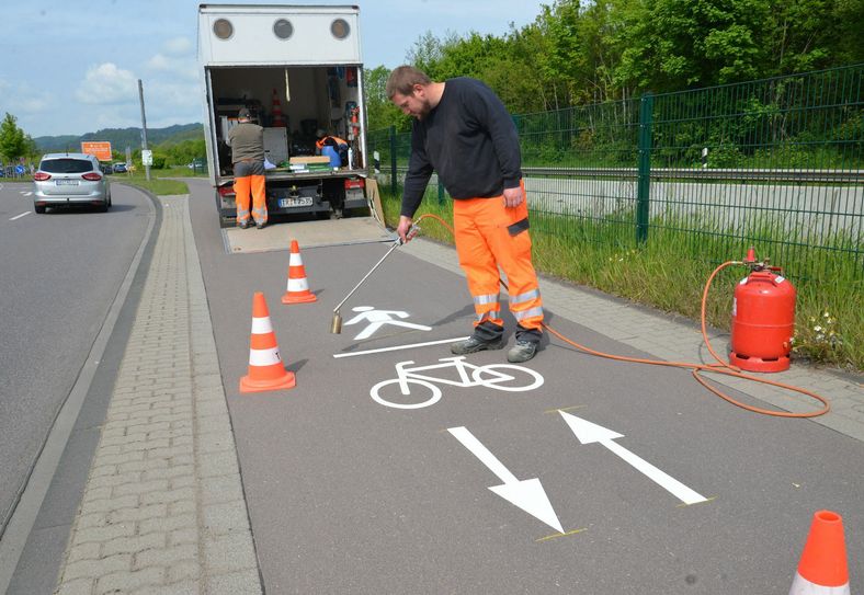 Martin Becker bringt das neue Piktogramm aus Heißplastik mit einem Gasbrenner auf den Geh- und Radweg entlang der Loebstraße auf. Foto: Presseamt Trier