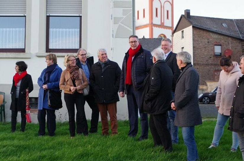 Von außen betrachtete Minister Alexander Schweitzer (m. rotem Schal) das Pfarrheim. Derzeit sind dort ukrainische Geflüchtet untergebracht, weshalb das Projekt noch nicht direkt angegangen wird.