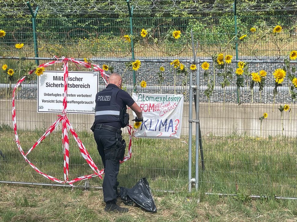 Polizeibeamte entfernen die Sonnenblumen, die von den Demonstranten am Zaun des Bundeswehrstandortes Büchel befestigt wurden.