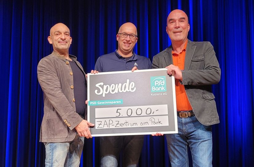"Die haben es verdient." - Kabarettist Django Asül, Thomas Biersch, Geschäftsführer des Kulturkreises Region Emmelshausen, sowie Björn Engelmann, Vorstandsmitglied der PSD Bank Koblenz (v.l.n.r.), bei der Übergabe eines Spendenschecks der Bank im ZAP in Emmelshausen.