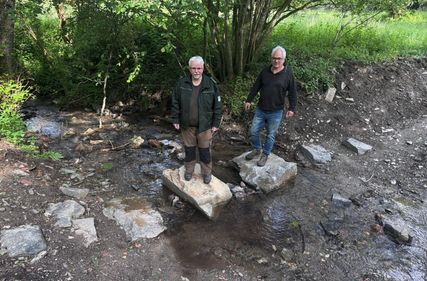 Markus Vollmer vom Bundesforstbetrieb Rhein-Weser (l.) und Eckhard Jäck, Leiter der Holzbauwerkstatt der Nationalparkverwaltung (r.) testen die neuen, naturbelassenen Trittsteine im erfolgreich renaturierten Bachbett des Sauerbachs.
