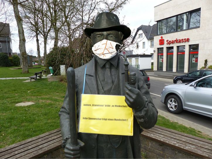 Auch Simmeraths Identifikationsfigur, der Kraremann, hat sich der Corona-Krise angepasst. Mit selbstgenähter Baumwollmaske grüßt er alle Besucher und animiert mit einem umgehängten Schild: »Jeddere Kraremann dräht ne Monkschotz!« Für diejenigen, die der Mundart nicht mächtig sind, ist die Übersetzung gleich beigefügt: »Jeder Simmerather trägt einen Mundschutz.« Foto: Hoffmann