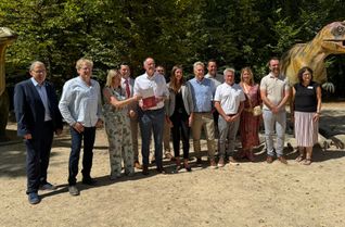 Wirtschafts- und Tourismusminister des Landes, Michael Ebling (5.v.l.) übergibt den Förderbescheid an die Felsenland Südeifel Tourismus GmbH im Dinosaurierpark in Ernzen.