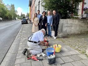 Frank-Matthias Mann verlegt die Stolpersteine. Im Hintergrund verfolgen Mitglieder des Kollegiums, Schulleiterin Alexandra Birk-Märker, Oberbürgermeister Dirk Meid und Landrat Marko Boos die Zeremonie.