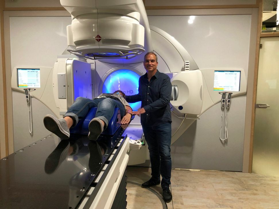 Dr. med Guido Syré und eine Mitarbeiterin demonstrieren, wie ein Patient bei der Behandlung unter dem Linearbschleuniger liegt. Fotos: J. Urban