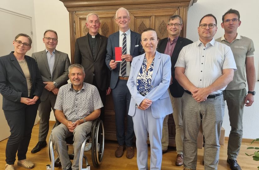 OB Wolfram Leibe (hinten Mitte) präsentiert nach dem Gespräch die ihm überreichte symbolische rote Tür der Jahreskampagne 2025 der Caritas. Die Stadtverwaltung wurde außerdem vertreten durch Bürgermeisterin Elvira Garbes (vorn Mitte) sowie Jugendamtsleiter Carsten Lang und Sozialamtsleiter Björn Borkenhagen (v. r.). Für die Caritas waren die beiden Trierer Direktoren Annemarie Egner und Christian Nicolay dabei sowie Helmut Müller, Vorsitzender SKM-Diözesanverein, Domkapitular Benedikt Welter, Vorsitzender des Caritasverbands der Diözese Trier, sowie Diözesan-Caritasdirektor Christoph Wutz (v. l.).