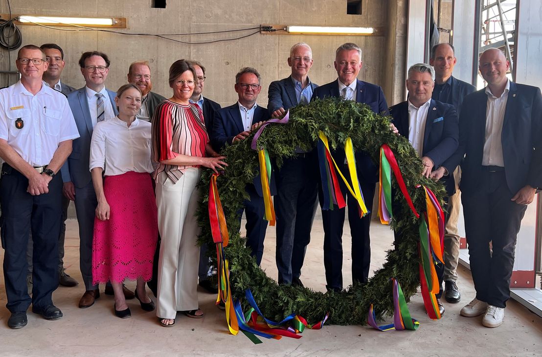 Großer politischer Bahnhof zum Richtfest: der Trierer Feuerwehr-Chef Andreas Kirchartz (l.), Trierer Oberbürgermeister Wolfram Leibe (5.v.r.) und Dezernenten, Landräte der beteiligten Landkreise und Ministerpräsident Gordon Schnieder (4.v.r.) mit dem Richtkranz