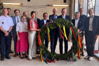 Großer politischer Bahnhof zum Richtfest: der Trierer Feuerwehr-Chef  Andreas Kirchartz (l.), Trierer Oberbürgermeister Wolfram Leibe (5.v.r.) und Dezernenten, Landräte der beteiligten Landkreise und Ministerpräsident Gordon Schnieder (4.v.r.) mit dem Richtkranz