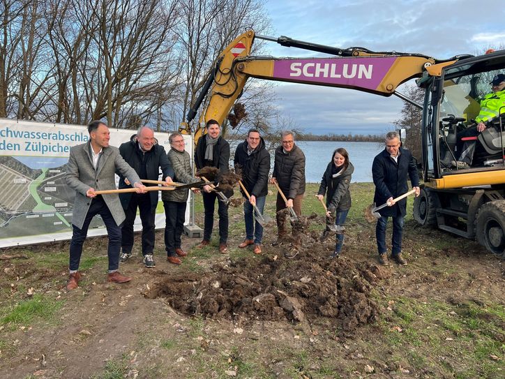 Griffen zum Spaten (v.l.): Joachim Franzen (Stadt Zülpich, Geschäftsbereichsleiter Tiefbau), Professor Heinrich Schäfer (Erftverband, Vorstand), Ottmar Voigt (Stadt Zülpich, Wiederaufbaubeauftragter), Michael Höhn (Stadt Zülpich, Allgemeiner Vertreter des Bürgermeisters), Marcel Schneider (Kreis Euskirchen, Untere Wasserbehörde), Ulf Hürtgen (Stadt Zülpich, Bürgermeister), Ronja Wenselau (Erftverband, Projektleiterin) und Dr. Peter Kramp (Stadt Zülpich, Wiederaufbauberater).