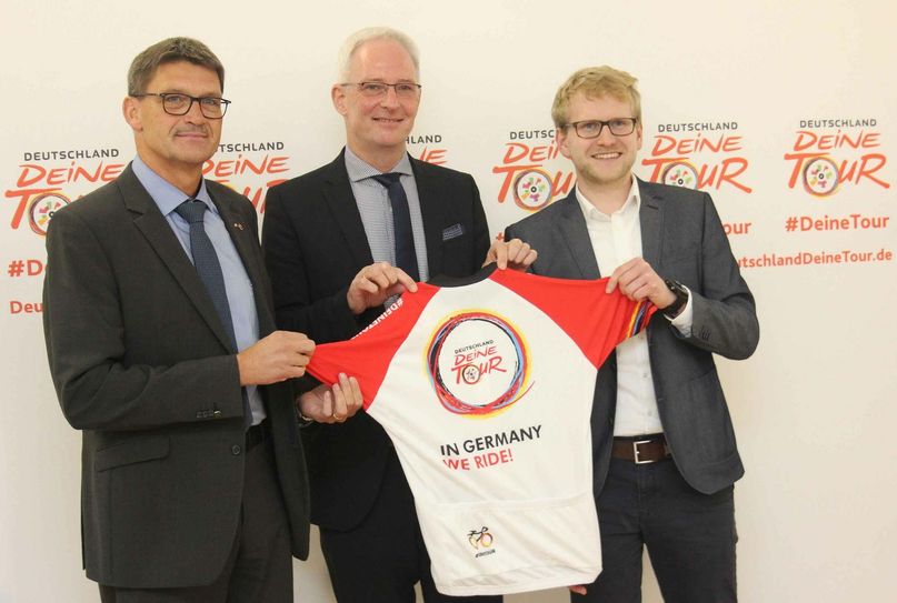 OB Wolfram Leibe (Mitte) und Landrat Günther Schartz (l.) präsentieren mit Matthias Pietsch, Projektmanager des Veranstalters ASO (r.), das offizielle Trikot der Deutschland-Tour 2018. Foto: Presseamt Stadt Trier