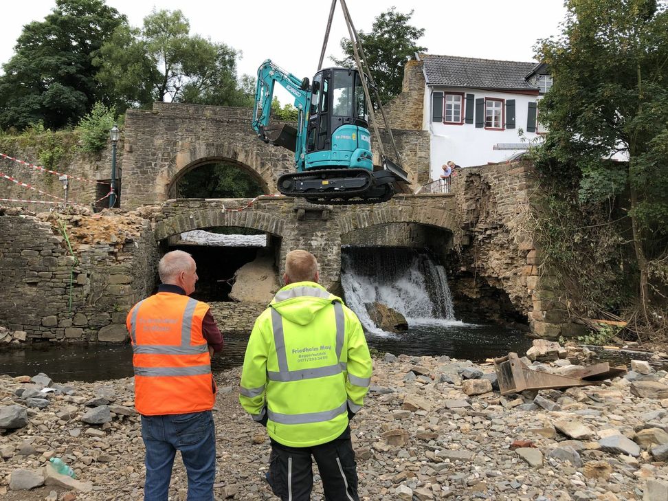 Peter Schneider aus Harzheim (li.) und Simon Esch aus Pesch erwarten ihre Arbeitsgeräte, die ein 350 Tonnen schwerer Kran ins Bachbett der Erft in Bad Münstereifel über die Stadtmauer hievte. mn-Fotos