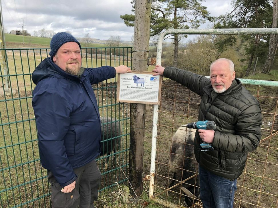 Bei seinem Besuch in der Eifel hatte Dr. Jürgen Günterschulze (re.) einiges im Gepäck. Hier bringt er mit Arnim Petralla die Hinweistafel zum Guteschaf an.