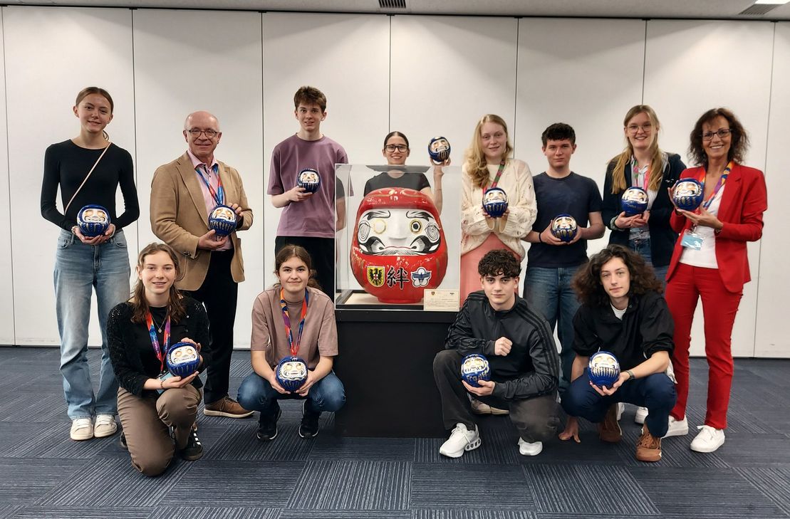 Daruma-Puppen sind die bekanntesten japanischen Glücksbringer. Das Gruppenfoto zeigt außerdem den großen roten Daruma, der im Rahmen des 50-jährigen Städtepartnerschaftsjubiläums 2015 erstellt wurde.