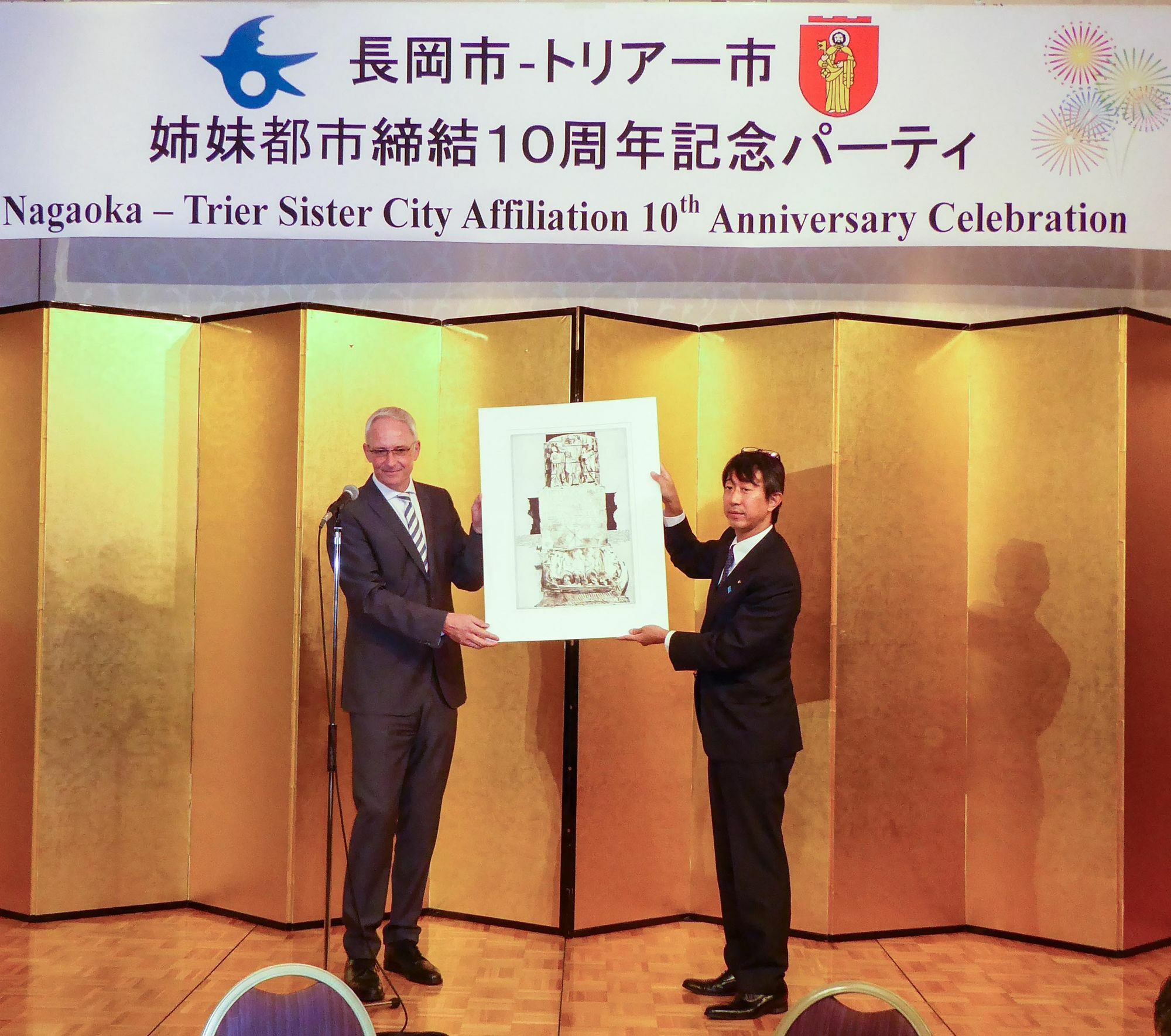OB Wolfram Leibe überreicht Nagaokas Bürgermeister Shinji Takami bei der Jubiläumsfeier im Nagaoka Grand Hotel eine Grafik von Klaus Swoboda als Gastgeschenk. Foto: Stadt Trier