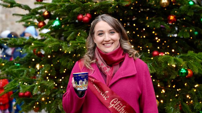 Louisa Kress, Deutsche Glühweinkönigin, mit einer Tasse Winzerglühwein vor dem geschmückten Tannenbaum auf dem Trierer Weihnachtsmarkt.