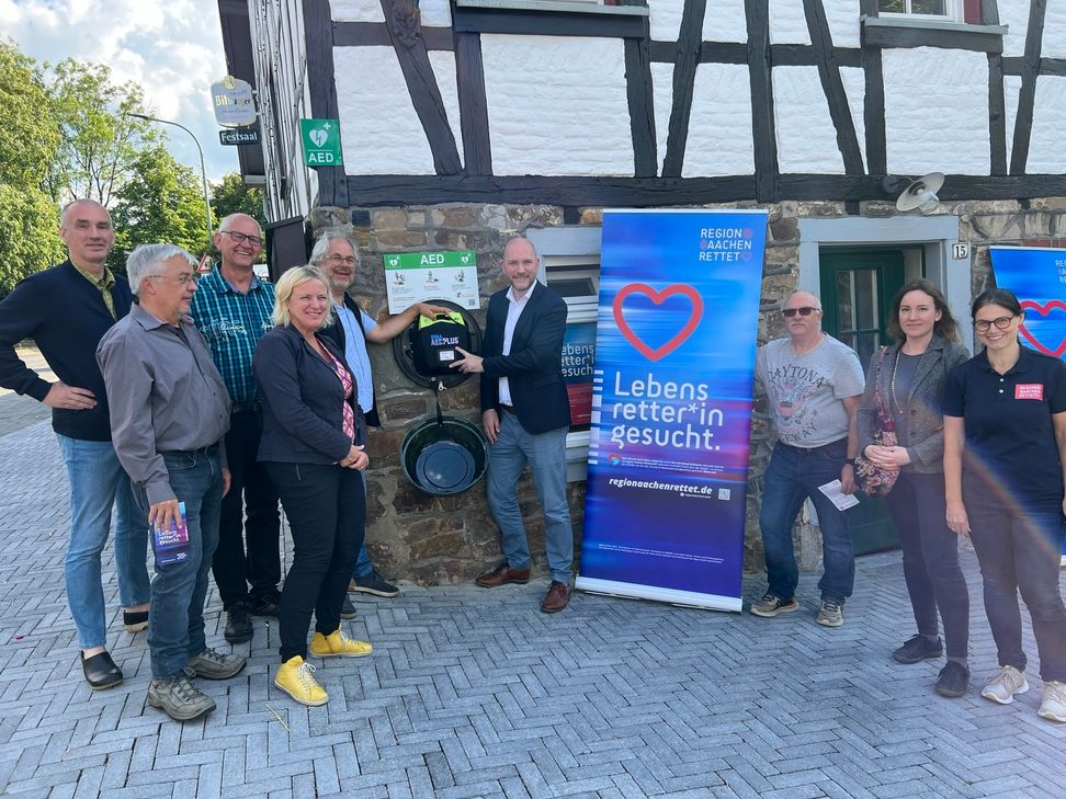 Vertreter des Förderverein »Saal Hütten«, der Initiative »Region Aachen rettet« sowie Bürgermeister Jorma Klauss präsentieren den »Automatisierten Externen Defibrillator«, der in Rotter Dorfmittelpunkt jederzeit für den Notfall öffentlich zugänglich ist. Foto: T. Förster