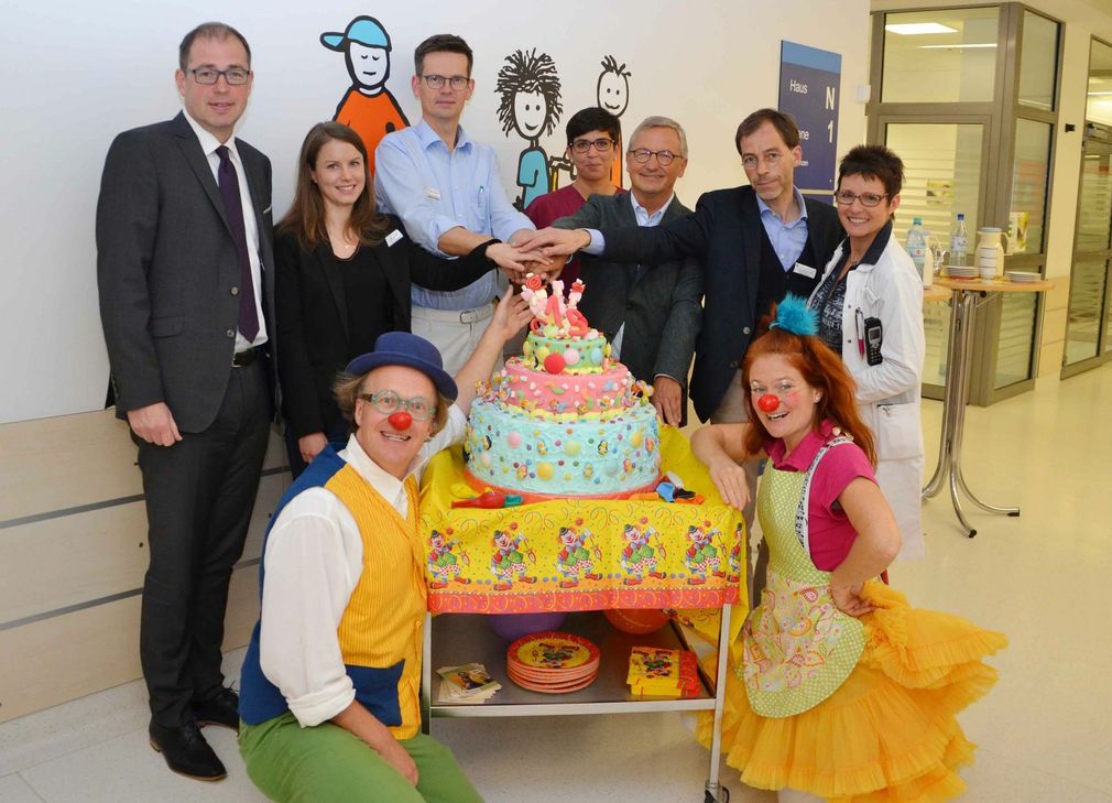 Die Clowns Lolek und Tilotamma feiern ihren 15. Geburtstag im Klinikum Mutterhaus. Gemeinsam schneiden sie eine große Geburtstagstorte an: Geschäftsführer Jörg Mehr (links) das Team des Kinderzentrums Klinikums Mutterhaus, Dr. Manfred Bitter von der Herbert & Veronika Reh-Stiftung (3. von rechts hinten). Foto: Kristina Kattler