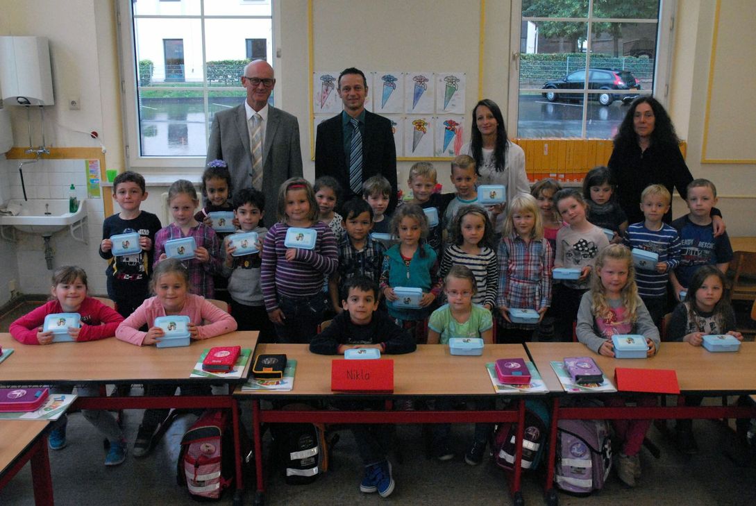 Bild: Über die von RWE Deutschland mitgebrachten Brotdosen freuten sich die Kinder der Grundschule in Kasel gemeinsam mit dem Bürgermeister der Verbandsgemeinde Ruwer Bernhard Busch, Marco Felten von RWE Deutschland, Klassenlehrerin Jennifer Kirsten und Schulleiterin Sonja Sommer (hintere Reihe, v.l.).