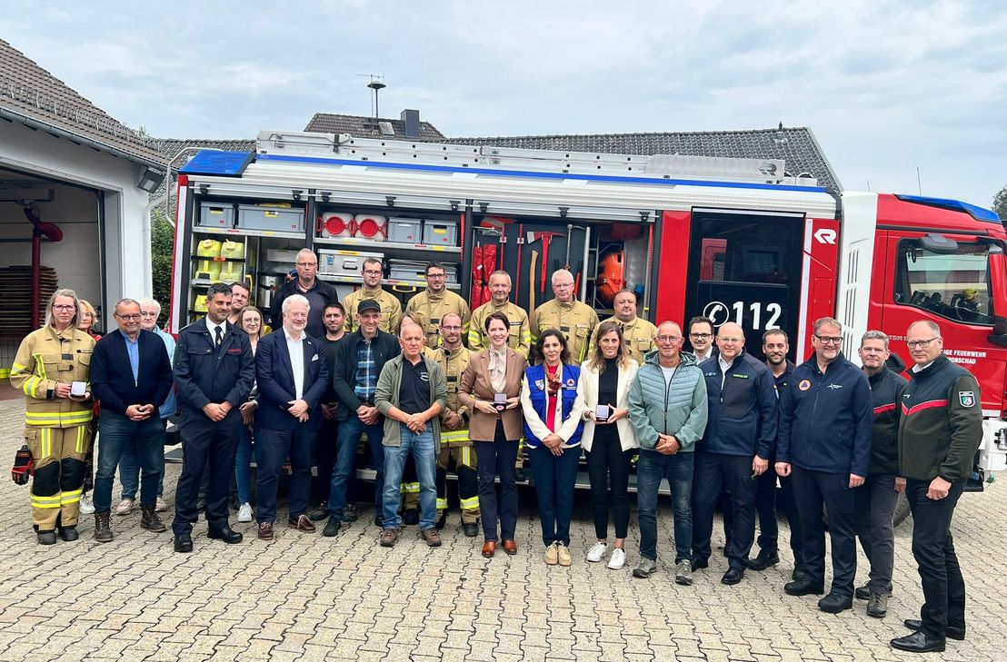 EU-Kommissarin Hadja Lahbib inmitten von NRW-Landwirtschaftsministerin Silke Gorißen, Monschaus Bürgermeisterin Dr. Carmen Krämer, den Einsatzkräften aus Feuerwehr und THW sowie vielen Helfern im Hintergrund am Kalterherberger Feuerwehrhaus.