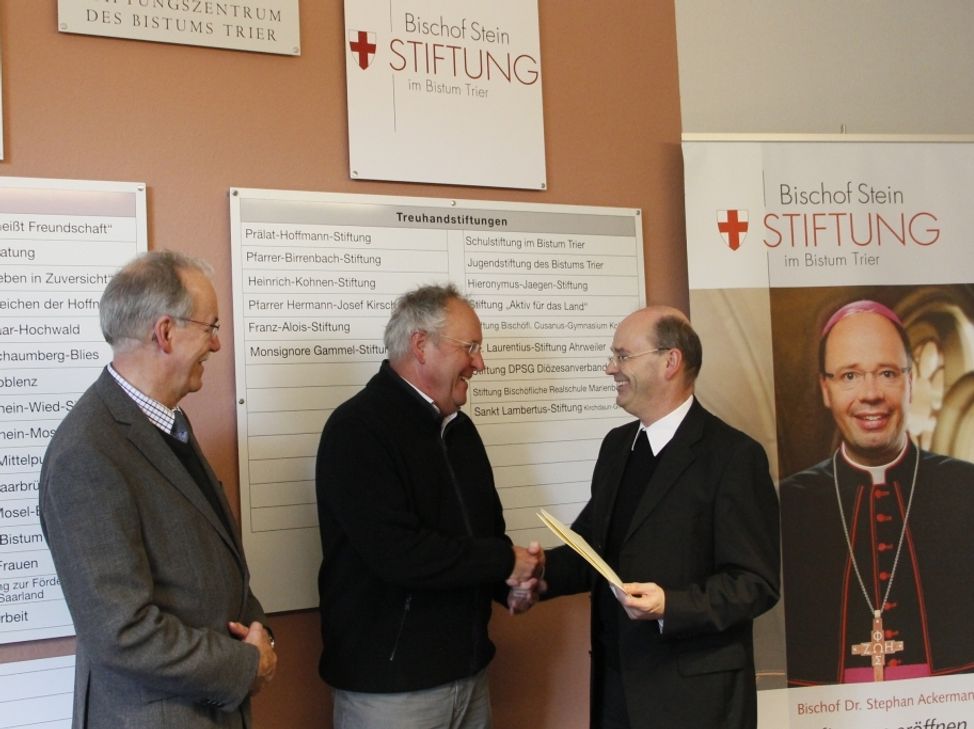 Weihbischof Robert Brahm (rechts) übergibt die Ernennungsurkunde an Johannes Becker-Laros (Mitte). Links daneben der Leiter des Stiftungszentrums, Winfried Görgen. Foto: Bistum