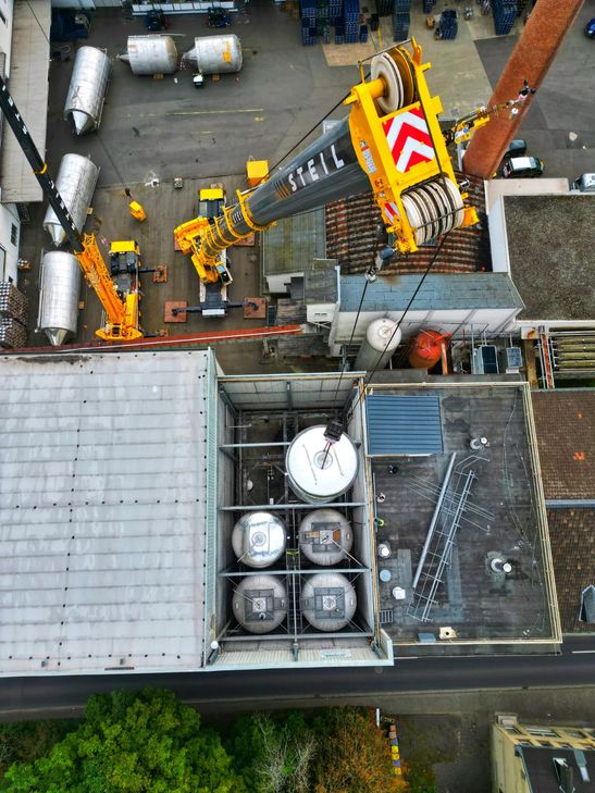 Millimeterarbeit in luftiger Höhe: Zwei Spezialkräne hieven neue Edelstahltanks in die Produktionshalle der Kirner Brauerei.