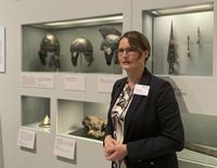 Kuratorin Dr. Silva Bruder vor römischen Eisen-Helmen und Waffen