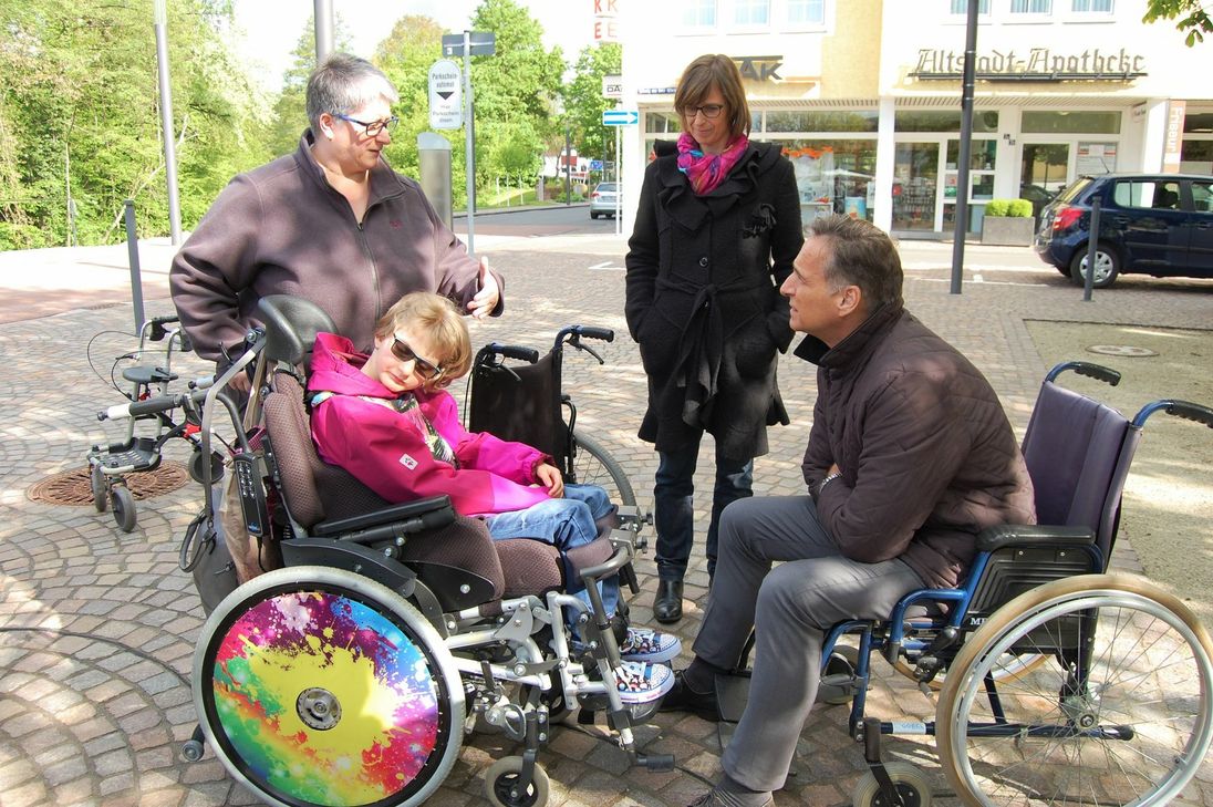 Bürgermeister Joachim Rodenkirch probiert einen Rollstuhl aus, fährt über den Platz und hört sich die Sorgen von Tammy Kayser (links), Mutter von Roxanne und Ilona Klein (rechts) an. Foto: Urban