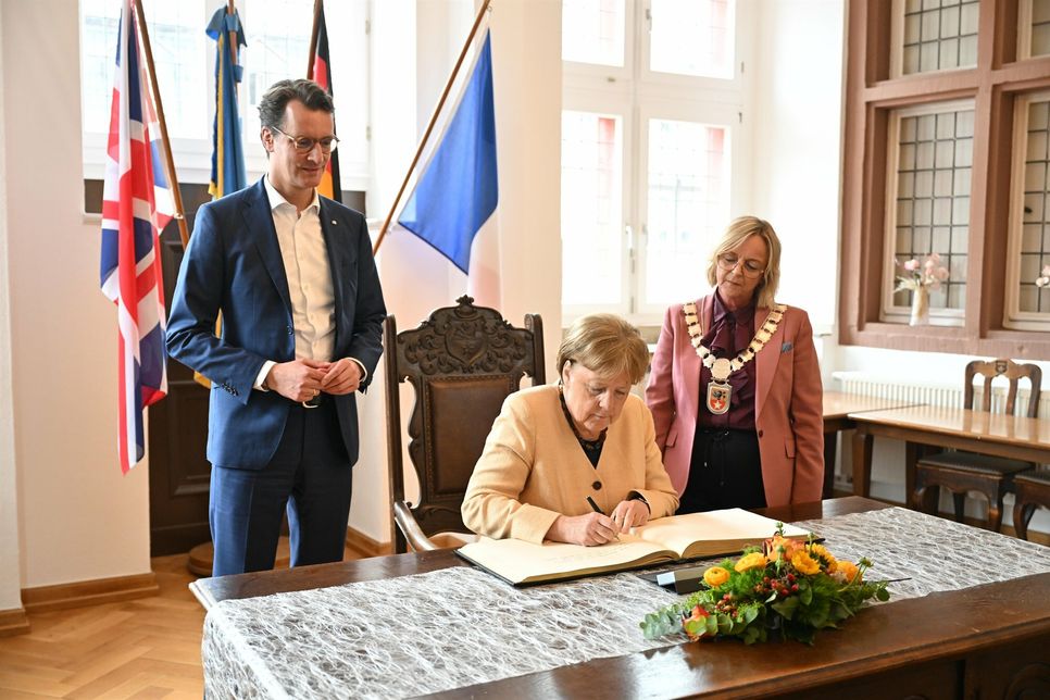 Die frühere Kanzlerin Angela Merkel (Mitte) trug sich im Beisein von NRW-Ministerpräsident Hendrik Wüst (li.) und Bürgermeisterin Sabine Preiser-Marian in das goldene Buch der Stadt ein.