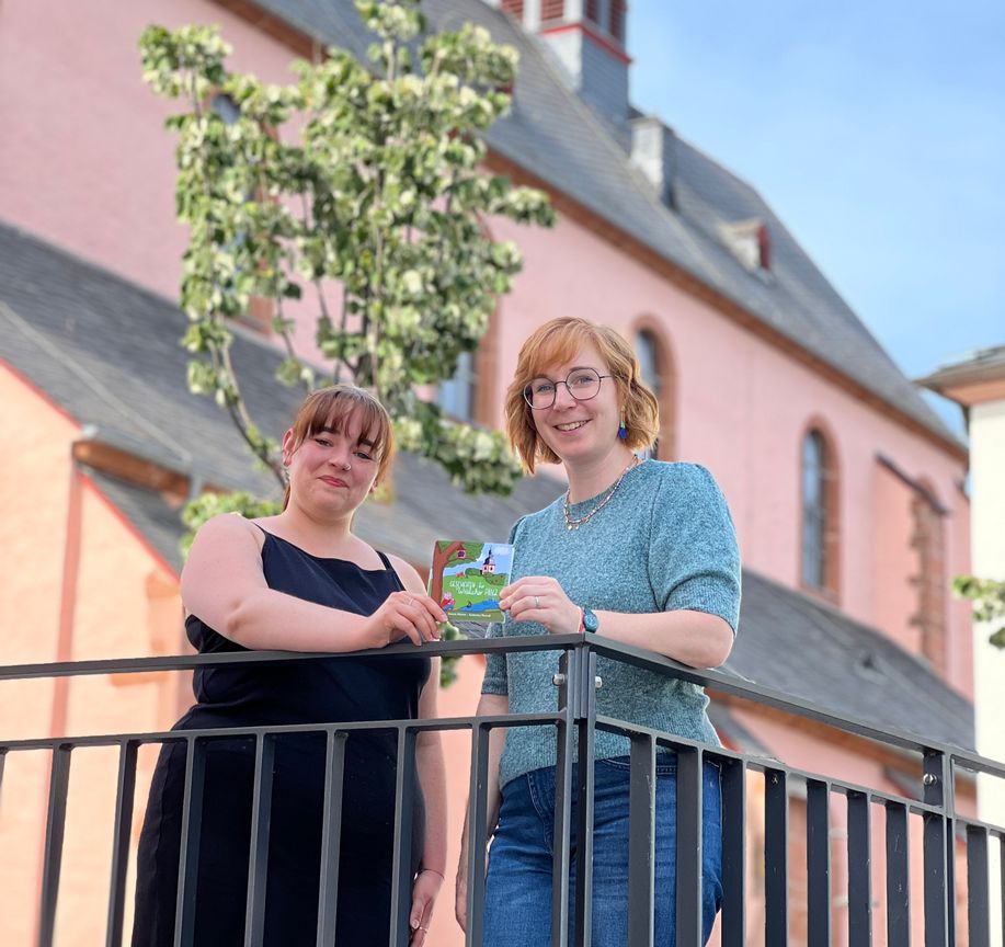 Vor der Markuskirche präsentieren Autorin Jasmin Dietzen (li.) und Illustratorin Katharina Thewalt ihr neues Kinderbuch. Viele Schauplätze und liebevolle Details aus Wittlich finden sich in den Geschichten und Bildern wieder.