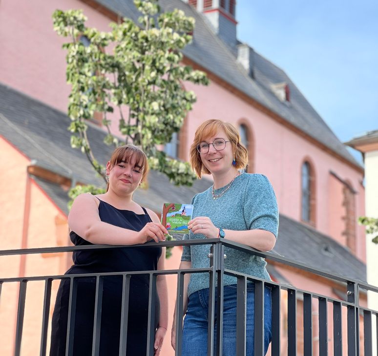 Vor der Markuskirche präsentieren Autorin Jasmin Dietzen (li.) und Illustratorin Katharina Thewalt ihr neues Kinderbuch. Viele Schauplätze und liebevolle Details aus Wittlich finden sich in den Geschichten und Bildern wieder.