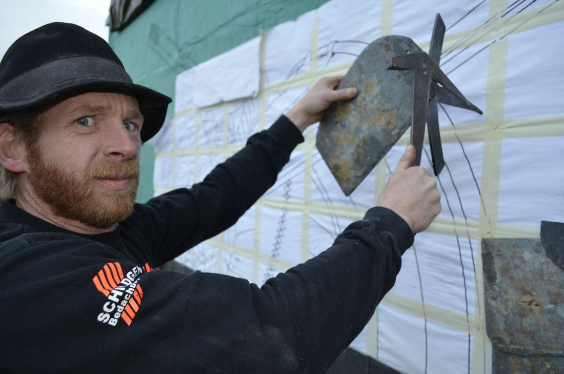 Klassische Handwerkskunst: Der Schiefer wird von Sascha Schildgen alleine mit dem Schieferhammer und der Haubrücke bearbeitet. Es braucht schon viel handwerkliches Geschick, den Schiefer an den gewünschten Stellen zu brechen. Anhand einer Vorlage fügt der Dachdecker dann den behauenen Schiefer zu einem Ornament zusammen.