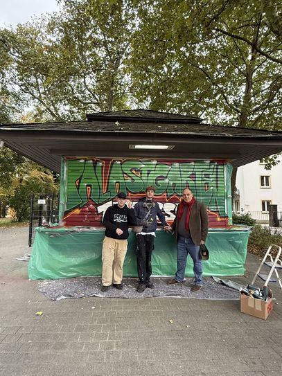 Die Künstler Mark Szücs und Carlo Mazzucco präsentieren zusammen mit Pächter Niels Becker ihr gestaltetes Graffiti an den Rollläden des Palastgarten Kiosks.