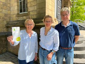 Engagieren sich im Projekt »Unterwegs zu Menschen« der evangelischen Sophiengemeinde Euskirchen (v.li.): Die Ehrenamtler Karin Domschke (li.), die einen Flyer des Projekts präsentiert, und Stephan Glauch (re.). Koordiniert werden die ehrenamtilichen Einsätze von Iris Hoffmann (Mitte).