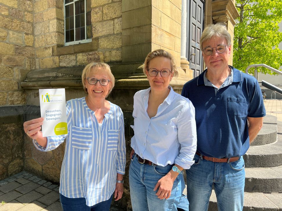 Engagieren sich im Projekt »Unterwegs zu Menschen« der evangelischen Sophiengemeinde Euskirchen (v.li.): Die Ehrenamtler Karin Domschke (li.), die einen Flyer des Projekts präsentiert, und Stephan Glauch (re.). Koordiniert werden die ehrenamtilichen Einsätze von Iris Hoffmann (Mitte).