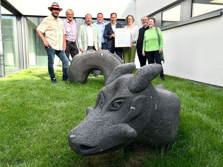 Sie begrüßen den Drachen „Grünling“ in der Kita in Konz-Könen - (v.l.) Künstler Guido Krämer, der städtische Beigeordnete Bernd Marx, der stellvertretende Ortsvorsteher Peter Rotthaus, der Gesamtleiter der Katholischen KiTa gGmbh Trier, Martin Roß, der Hauptamtliche Beigeordnete Guido Wacht, die Kita-Standortleiterin Rita Kurz sowie die Eltern des kurzfristig erkrankten Künstlers Alexander May.