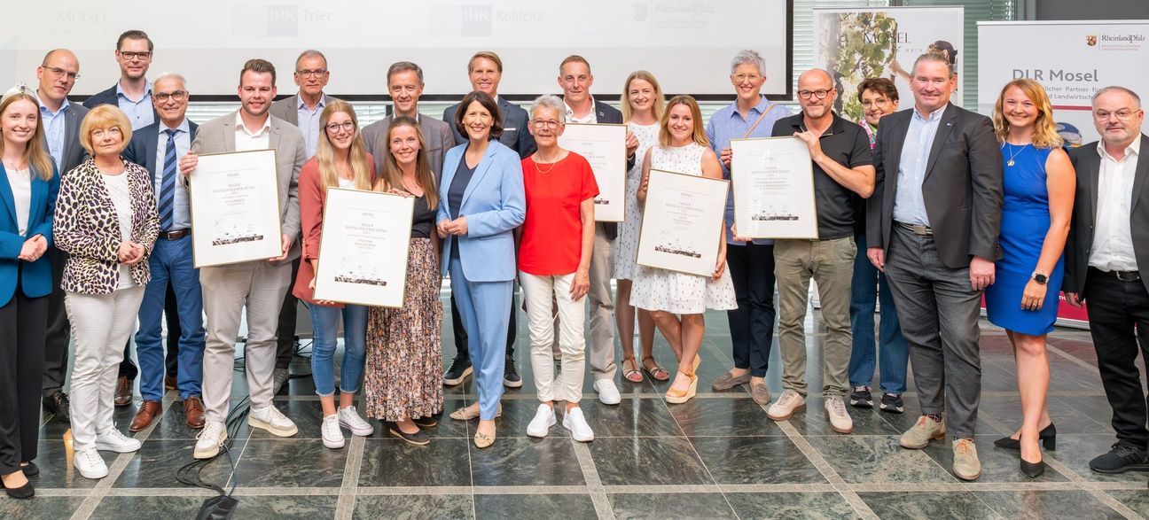 Die besten Weingastgeber Mosel 2025 freuen sich mit Ministerin Daniela Schmitt (Mitte), Mosel-Weinkönigin Anna Zenz (links) sowie den Vertretern der Wettbewerbsträger und Preisstifter über ihre Auszeichnung.